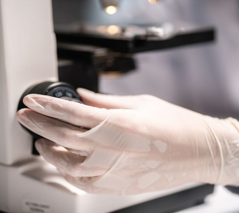 Scientist working with a microscope in a medical research lab, emphasizing advanced quality control for bacteriophage solutions at Qeen Biotechnologies.